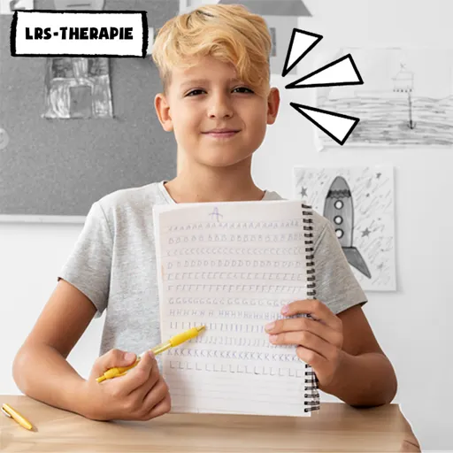 Bild zeigt - zum Thema: was ist integrative Lerntherapie - frontal Jungen, der an einem Schreibtisch sitzt. Er zeigt stolz, was er eben selbst geschrieben hat und deutet mit seinem Kugelschreiber darauf.